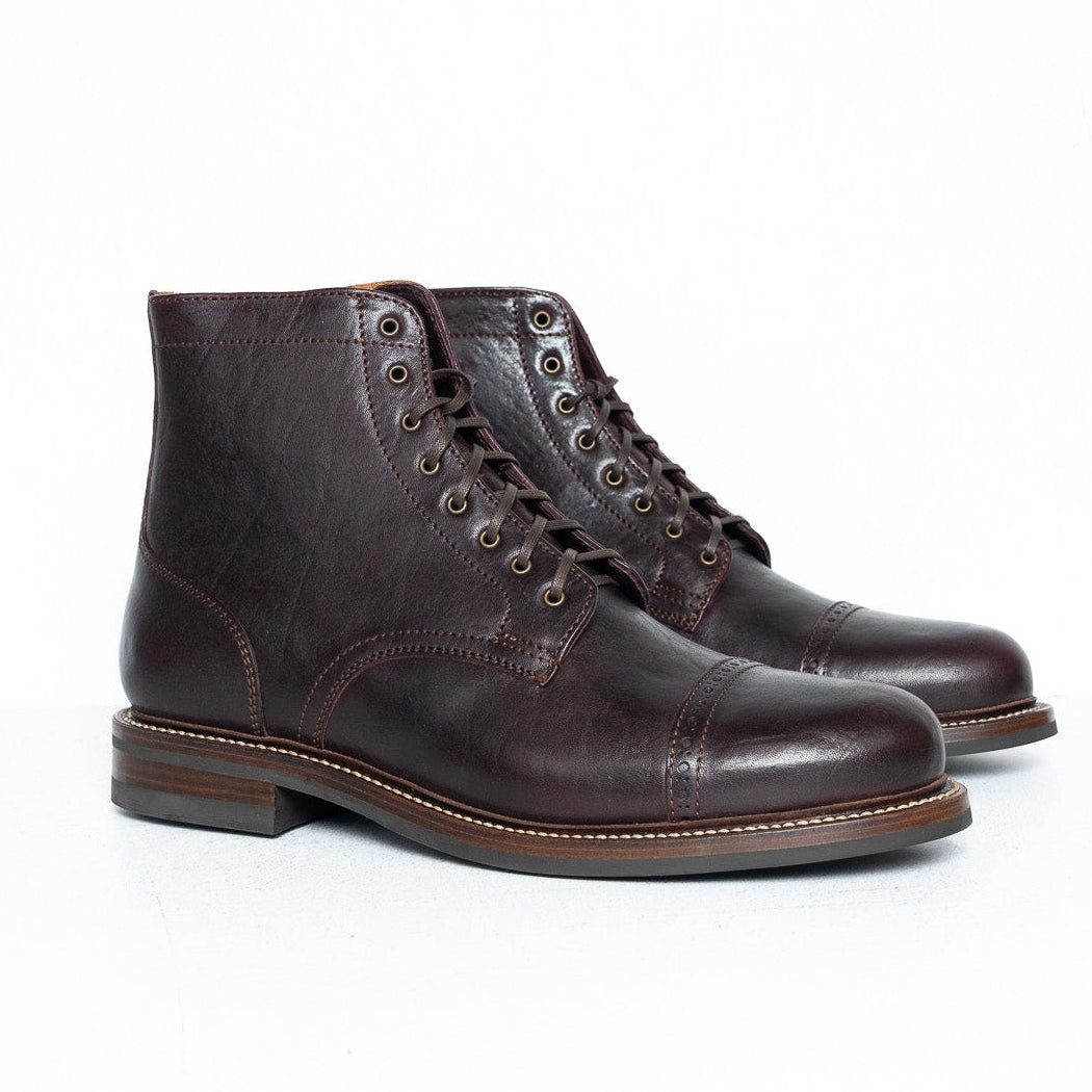 A pair of dark brown leather lace-up ankle boots with a cap toe and stacked heels, photographed on a clean white studio surface.